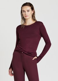 Burgunderfarbener Strickpullover mit langen Ärmeln, Rundhalsausschnitt und gerippten Manschetten, kombiniert mit passenden, figurbetonten Hosen mit Knopfdetail.