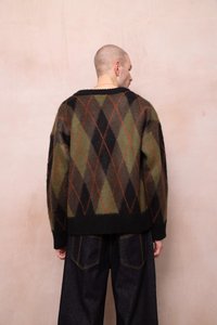 Megztinis su deimanto raštu tamsiai žalia, juoda ir ruda spalvomis, akcentuotas oranžinėmis linijomis; laisvas siluetas ir ilgos rankovės.