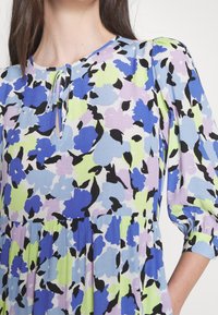 Florale jurk met een ronde halslijn, voorzien van een sleutelgatdetail. Kleuren zijn blauw, lavendel en groen. Gemaakt van lichte, gestructureerde stof.