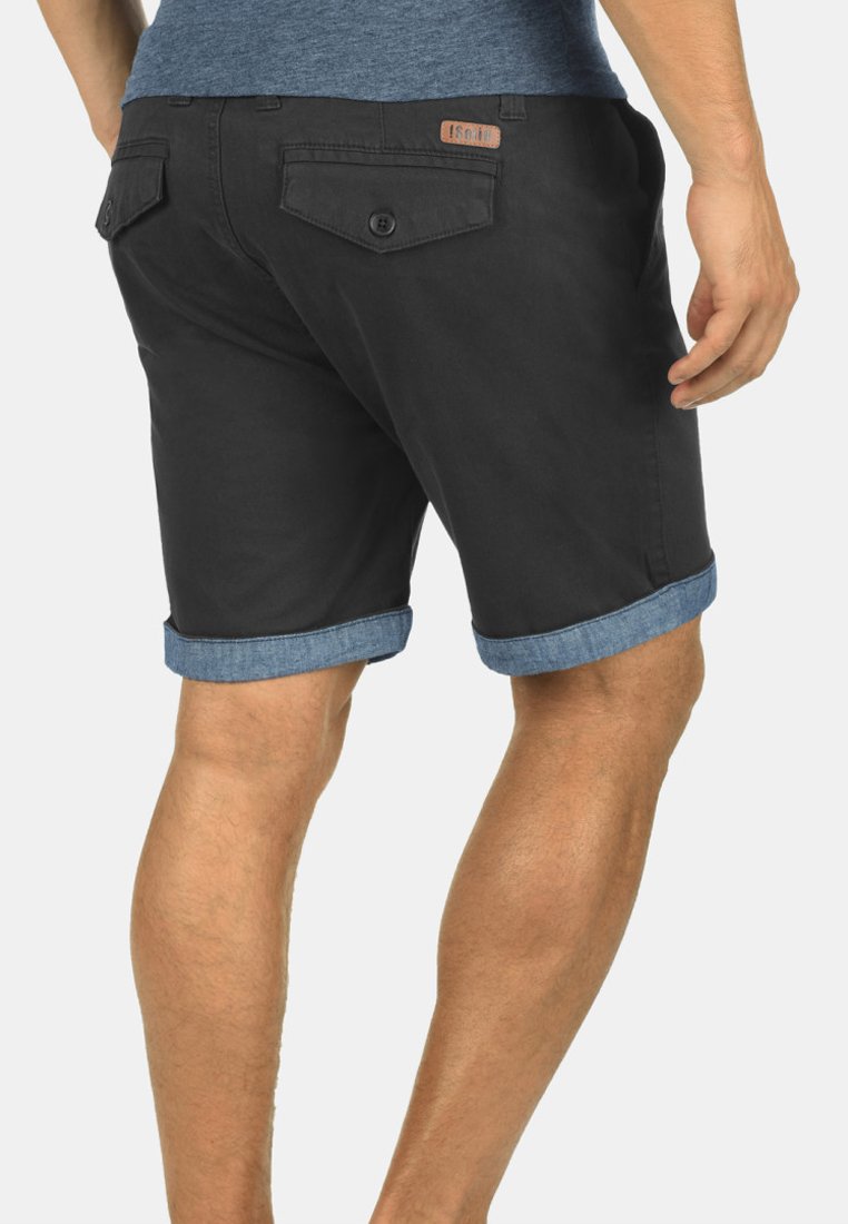 Svarta bomullsshorts med rullade denimkantar, försedda med två bakfickor med knappar och en läderlogotyp på midjebandet.