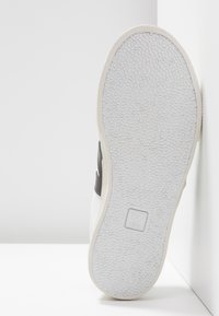 White sneakers with a textured rubber sole and gray accents. Features a logo on the sole and clean, minimalist design. Smooth leather upper.
