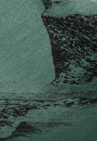 Tejido que presenta una tela verde texturizada con un diseño monocromático impreso de terreno rocoso y acantilados, resaltando la profundidad y el detalle.