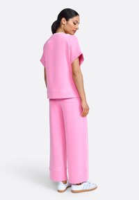 Roze oversized sweatshirt en wijde broek gemaakt van zacht materiaal. Bevat korte mouwen, ribgebreide zoom en een relaxte pasvorm. Witte sneakers getoond.