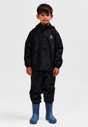 Sort vandtæt jakke med hætte, kombineret med matchende bukser og blå gummistøvler. Jakken har et logo på brystet.