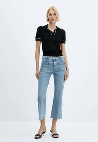 Camisa polo negra con bordes blancos, combinada con jeans cortos de color azul claro que presentan dobladillos deshilachados y bolsillos en la parte delantera y trasera. Llevado con tacones negros.