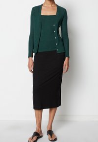 Musta midi-hame yhdistetty vihreään ribbineulottuun neulepaitaan, jossa on napit. Asussa on istuva siluetti ja sileä pinta.