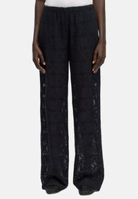 Zwarte haakgebreide broek met wijde pijpen en een ingewikkeld geometrisch patroon, voorzien van een elastische tailleband en een lichte textuur.