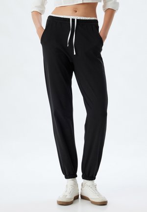 Zwarte joggingbroek van zachte stof, met een elastische tailleband met trekkoord, zijzakken en elastische boorden. Geschikt voor casual draagcomfort.