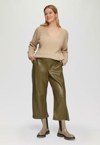 Beige gebreide trui met een V-hals, olijfgroene faux leren wijde broek en beige enkellaarsjes met zwarte accenten.