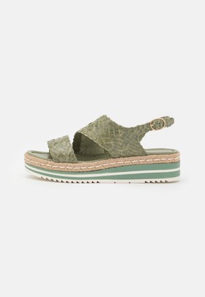 Groene gevlochten lederen sandaal met gekruiste banden, verstelbare enkelsluiting en een gestructureerde plateauzool met een gevlochten jute-accent.