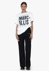 Witte oversized t-shirt met zwarte tekst "MARC ELLIS NEW YORK", gecombineerd met zwarte wijde broek, van gladde stof en met een casual ontwerp.