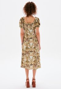 Blumengemustertes Midikleid aus leichtem Stoff; mit Puffärmeln und quadratischem Rückenausschnitt. Die Farbpalette umfasst Grün, Braun und Beige.
