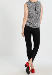 Ärmlös blus i svart och vitt mönster, kombinerad med svarta skinny jeans och röda klackskor. Märkbar dragkedja bak.