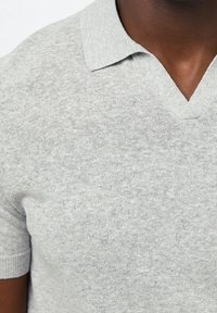 Polo gris à manches courtes avec un col en V. Confectionné en tissu tricoté texturé avec une finition douce. Dispose d'un col simple et discret.