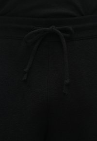 Czarne spodnie dresowe z regulowanym paskiem w pasie, gładką teksturą i miękkim wykończeniem tkaniny. Bez widocznych logo ani wzorów.