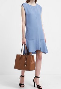Robe bleu clair au design simple, manches courtes, et deux poches avant. Sac fourre-tout en cuir marron avec ferrures dorées et logo. Talons noirs.