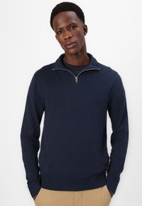 Dunkelblauer Pullover mit Reißverschlusskragen sowie gerippten Bündchen und Saum. Weicher Stoff, taillierte Passform und lange Ärmel.