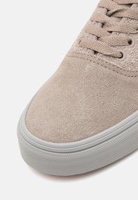 Baskets en suede beige avec des lacets assortis, semelle en caoutchouc blanc et paroi latérale texturée, présentées sur un fond blanc uni.