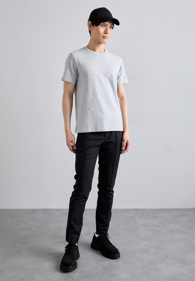 T-shirt en coton gris à manches courtes, pantalon noir ajusté, chaussures noires avec une surface texturée, et une casquette noire sur un fond neutre.
