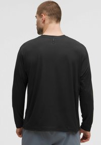 Maglietta nera a maniche lunghe realizzata in tessuto morbido. Caratterizzata da un colletto a girocollo e un'etichetta ad anello sul retro. Vestibilità casual e texture liscia.