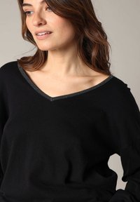 Pull en tricot noir avec un col en V et des bordures argentées. Texture douce et coupe décontractée, idéale pour un look casual.