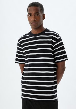 Camiseta de rayas blancas y negras con mangas cortas, escote redondo y tela de algodón suave. Presenta rayas horizontales audaces de diferentes anchos.