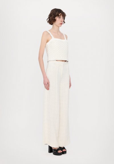 White textured crop top with square neckline and wide straps, paired with high-waisted, wide-leg pants in a similar material. Black platform sandals.