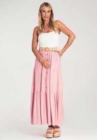 Rosa gestufter Maxikleid mit Knopfdetails, kombiniert mit einem weißen taillierten Tanktop und einem hellbraunen geflochtenen Gürtel. Weicher Stoff und lockere Passform.