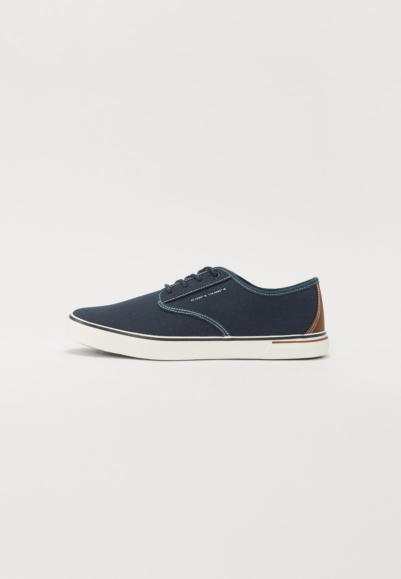 Zapatos de lona de color azul marino con un diseño de bajo perfil, que presentan acentos marrones, una suela de goma blanca y detalles de costura en contraste.