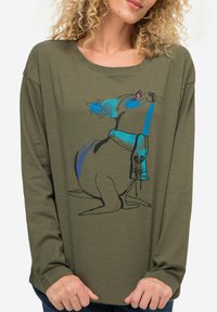 Oliwkowa koszula z długim rękawem z niebieskim i czarnym ilustrowanym wzorem królika. Miękka tkanina o luźnym kroju i szerokim dekolcie.