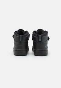 Svarta mid-top sneakers med slät yta, fleecefoder vid kanten och justerbart spänne. Har en sidologotyp och strukturerad gummisula.