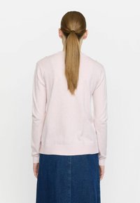 Ljusrosa tröja med långa ärmar, rund hals och ribbad nederkant, som bärs över en mörk denimkjol. Enfärgad struktur utan mönster.