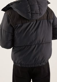 Puffjakke med en navy og sort farveskema, der har hætte, elastisk talje og glat tekstur. Bagside viser vandret syning.