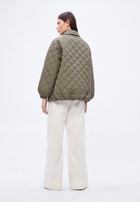 Prošívaná péřová bunda v černobéžovém vzoru kostkované lišky, s límcem a elastickými manžetami, nošená s krémovými širokými kalhotami.