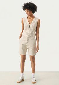 Beige ärmlös stickad topp med knappfront, i kombination med ljusgräddfärgade uppvikta shorts. Strukturell tygkvalitet och en avslappnad passform ingår.