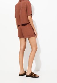 Haut à manches courtes couleur rouille et short assorti en tissu léger. Associés à des sandales plates à imprimé léopard marron et noir.