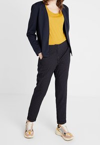 Námořnické sako, hořčicově žlutý top, černobíle pruhované kalhoty a vícebarevné tenisky s bílou podrážkou. Ležérní, moderní outfit.