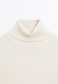 Pull à col roulé crème, fabriqué en tricot doux. Présente un col replié et des détails côtelés au niveau du cou et de l'ourlet.