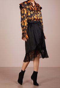Blouse en satin noir avec des motifs floraux orange et des accents volantés, associée à une jupe asymétrique noire avec des bordures en dentelle et des bottines.