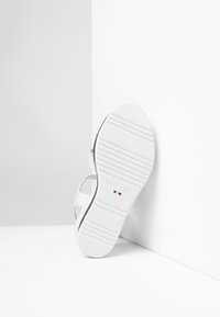 Sandalias blancas con suela plana de goma, que presentan tiras delgadas. La marca incluye "NeroGiardini" y "Hecho en Italia" grabadas en la suela.
