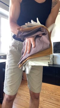 Stack of folded clothing in various colors: white, beige, brown, and cream. Fabric appears soft, with a smooth texture and no visible patterns.