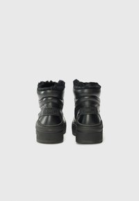 Bottes noires à talon avec doublure en fausse fourrure et cuir texturé, présentées par l'arrière, avec un logo bien visible sur le talon.