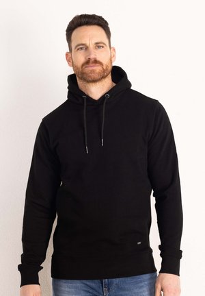 Felpa nera con cappuccio dotata di tasca frontale, cordino regolabile e polsini a costine. Indossata con jeans blu, esposta su uno sfondo bianco.
