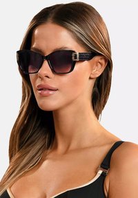 Czarne, oversize okulary przeciwsłoneczne z gradientowymi soczewkami, teksturowanymi akcentami po bokach oraz złotymi detalami. Prostokątna konstrukcja ramki.