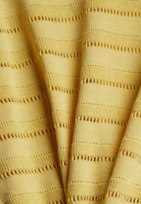 Pehmeän keltainen neulostekstiili, jossa on vaakasuoria raitoja avoimilla yksityiskohdilla. Rakenne on sileä ja siinä on vaihtelevia neulomismalleja.