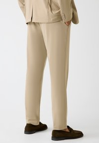 Beige pantalon van gladde stof met een getailleerde pasvorm, voorzien van zijzakken en gedragen met donkerbruine suède loafers.