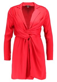 Robe blazer rouge à manches longues avec un détail ceinturé à la taille. Dotée d'un col à revers et d'un tissu lisse légèrement texturé.