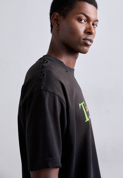 T-shirt negru supradimensionat cu o guler desfăcut și cusături decorative pe umăr. Prezintă un design colorat al textului pe față.