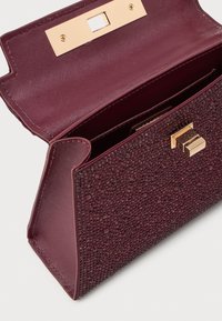 Geantă texturată burgundy cu un închizător auriu lucios, având o formă structurată și un interior neted. Potrivită pentru diverse ocazii.