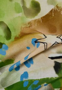 Stoff mit abstrakten grünen, braunen und blauen Pinselstrichen, der ein schwarzkonturiertes Sternmuster auf einem beigen Hintergrund zeigt.